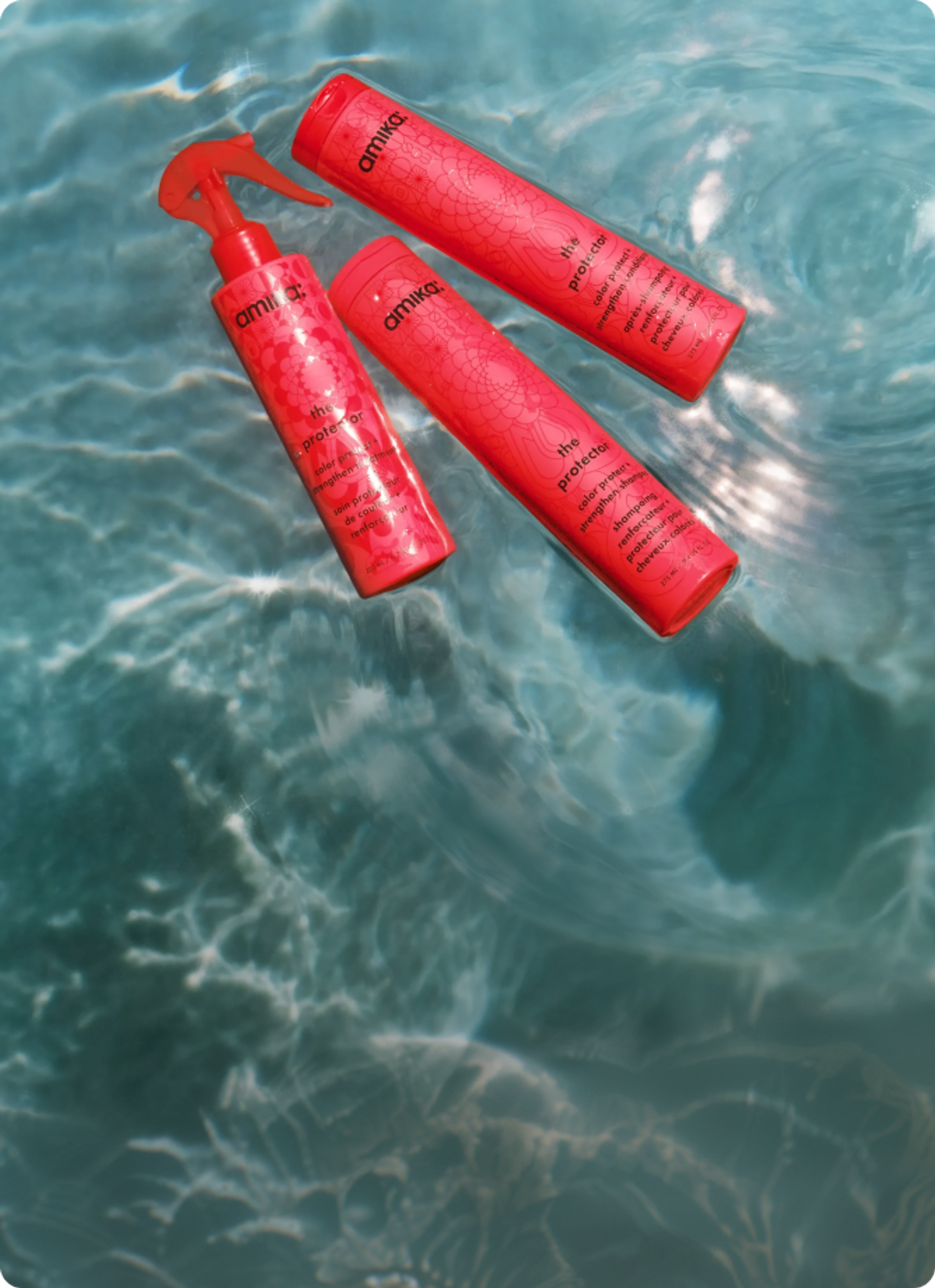 bottles of amika's the protector shampoo, conditioner, and treatment float in a swimming pool