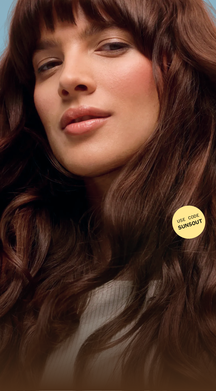 a brunette model with wavy hair stands against a blue background