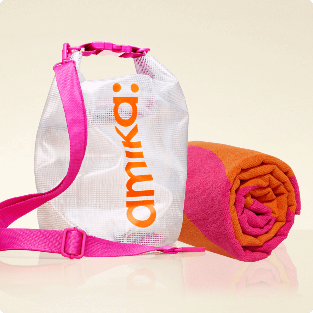 amika beach-ready bundle: an orange and pink towel rolled up next to a clear dry bag with pink strap and amika: logo in orange