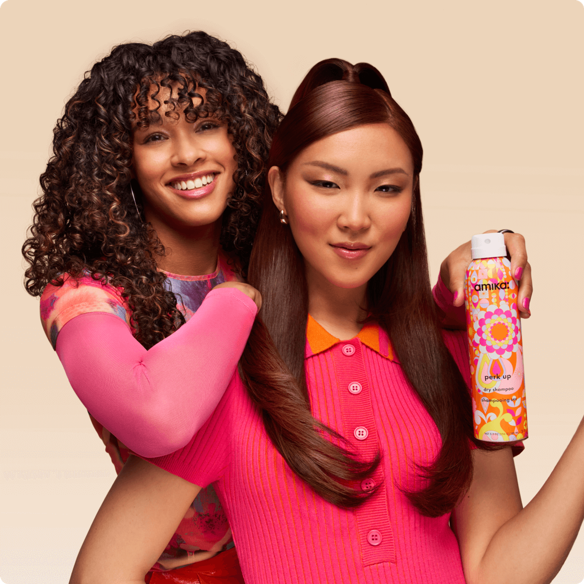 two models pose in front of a cream backdrop. one model holds a bottle of amika perk up dry shampoo
