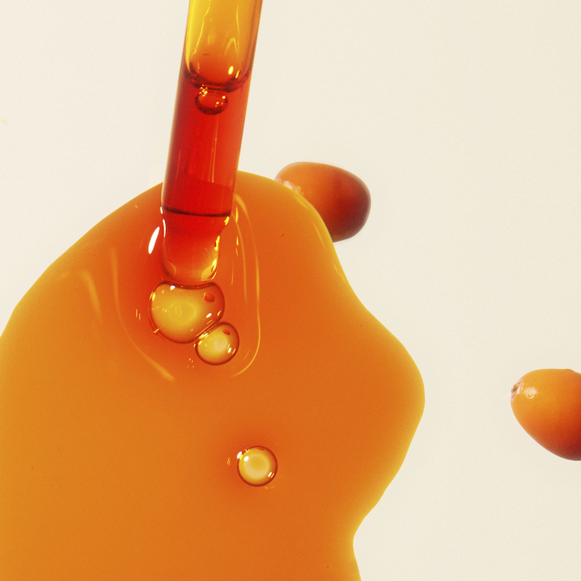 a dropper and a bit of sea buckthorn seed oil on a white background. 2 sea buckthorn berries are nearby