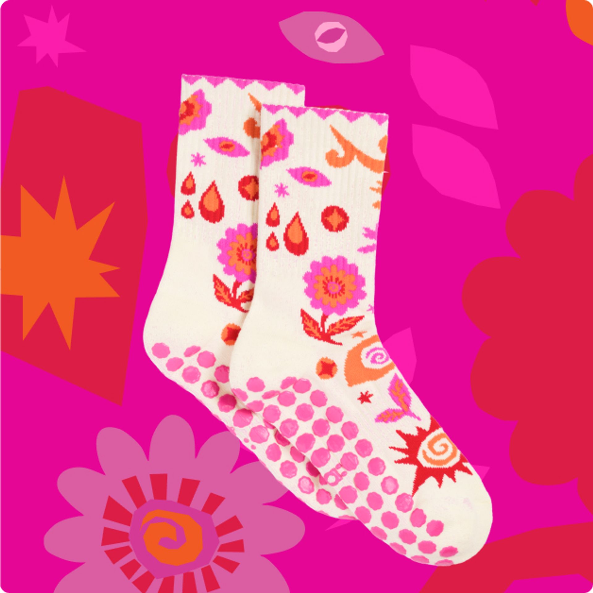 a pair of patterned socks with pink grips on the bottom against a pink, red, dark pink, and orange floral pattern.