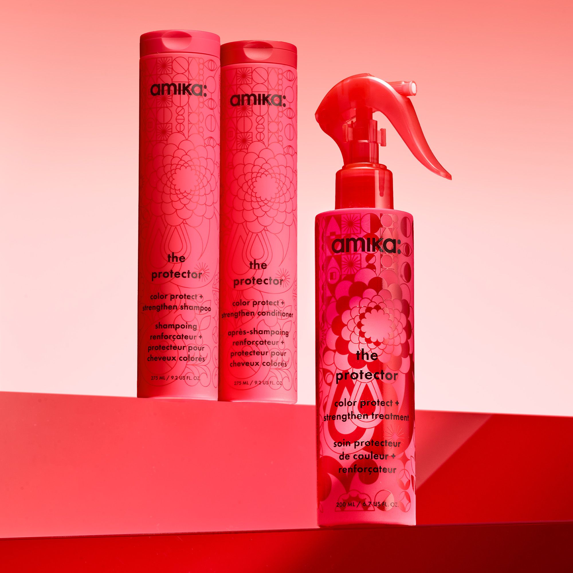 bottles of amika's the protector shampoo, conditioner, and treatment sit against a red gradient background