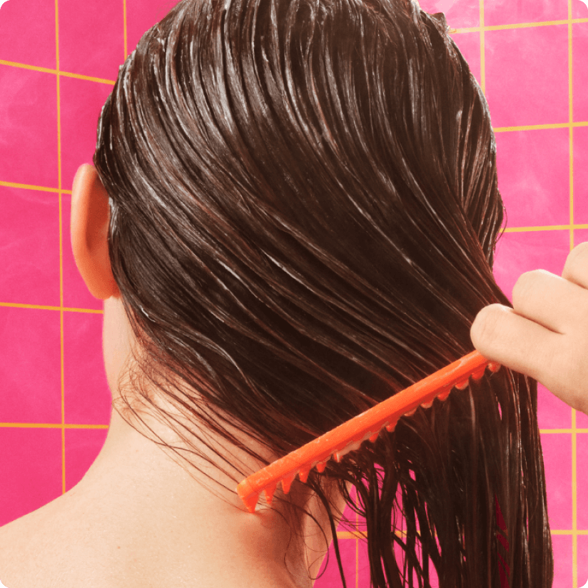 a model in a pink-tiled shower combs their wet hair with an orange comb