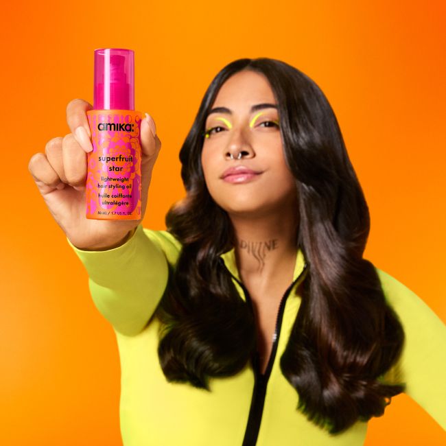 image shows a model holding a bottle of amika superfruit star oil out away from body