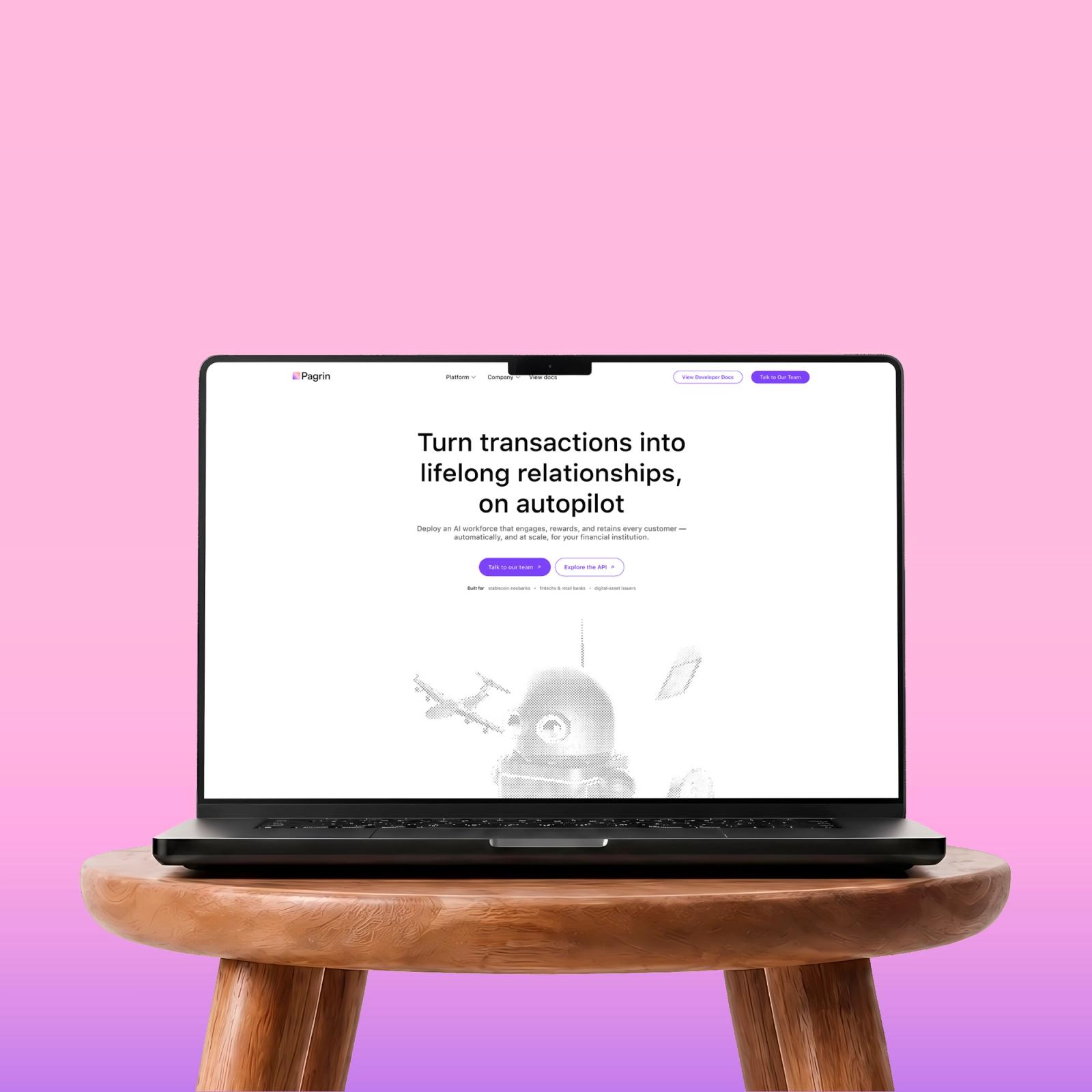The Pagrin homepage on a laptop resting on a wooden stool against pink.