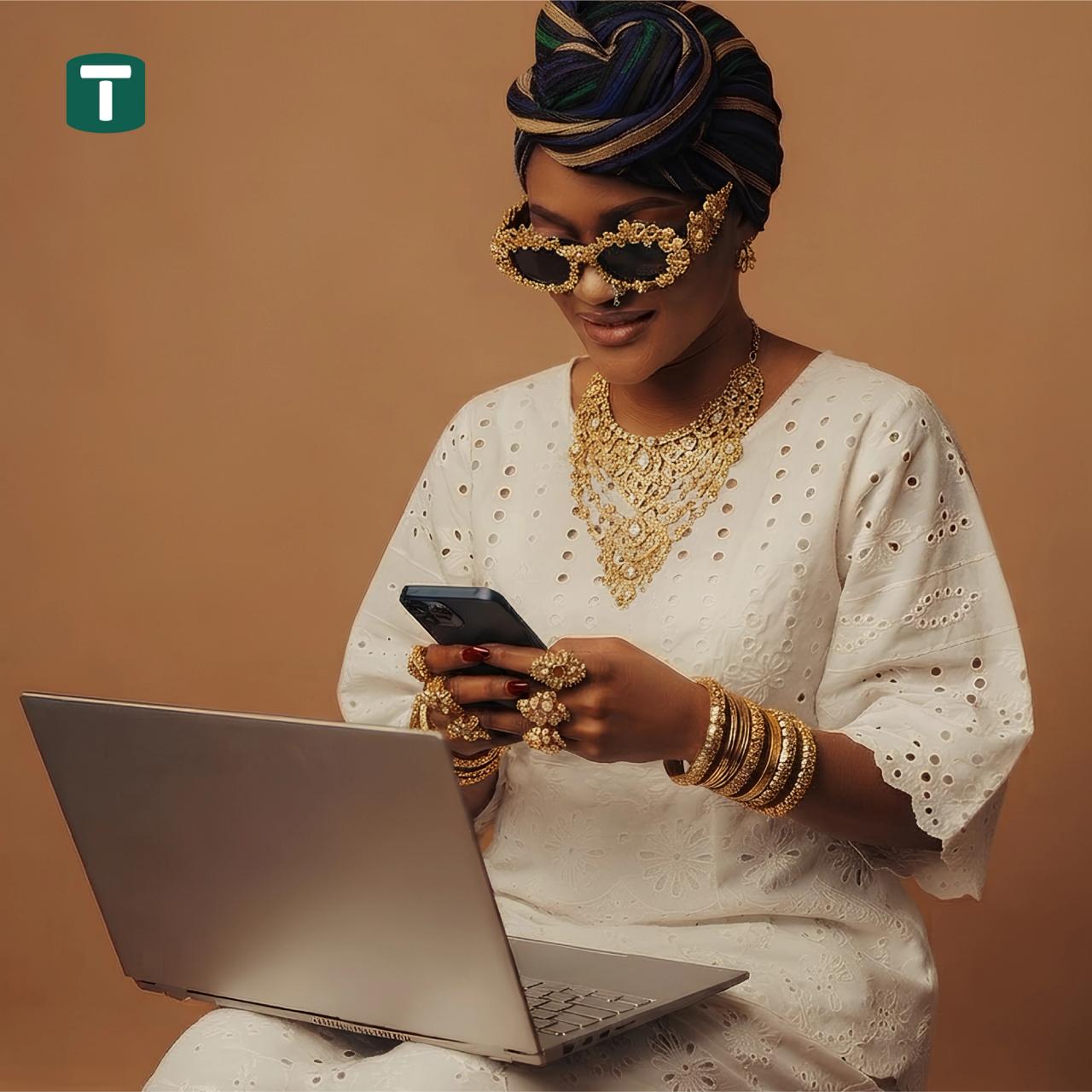 A woman in white eyelet fabric and gold jewellery using a phone beside a laptop, with the Tokkenly T mark.