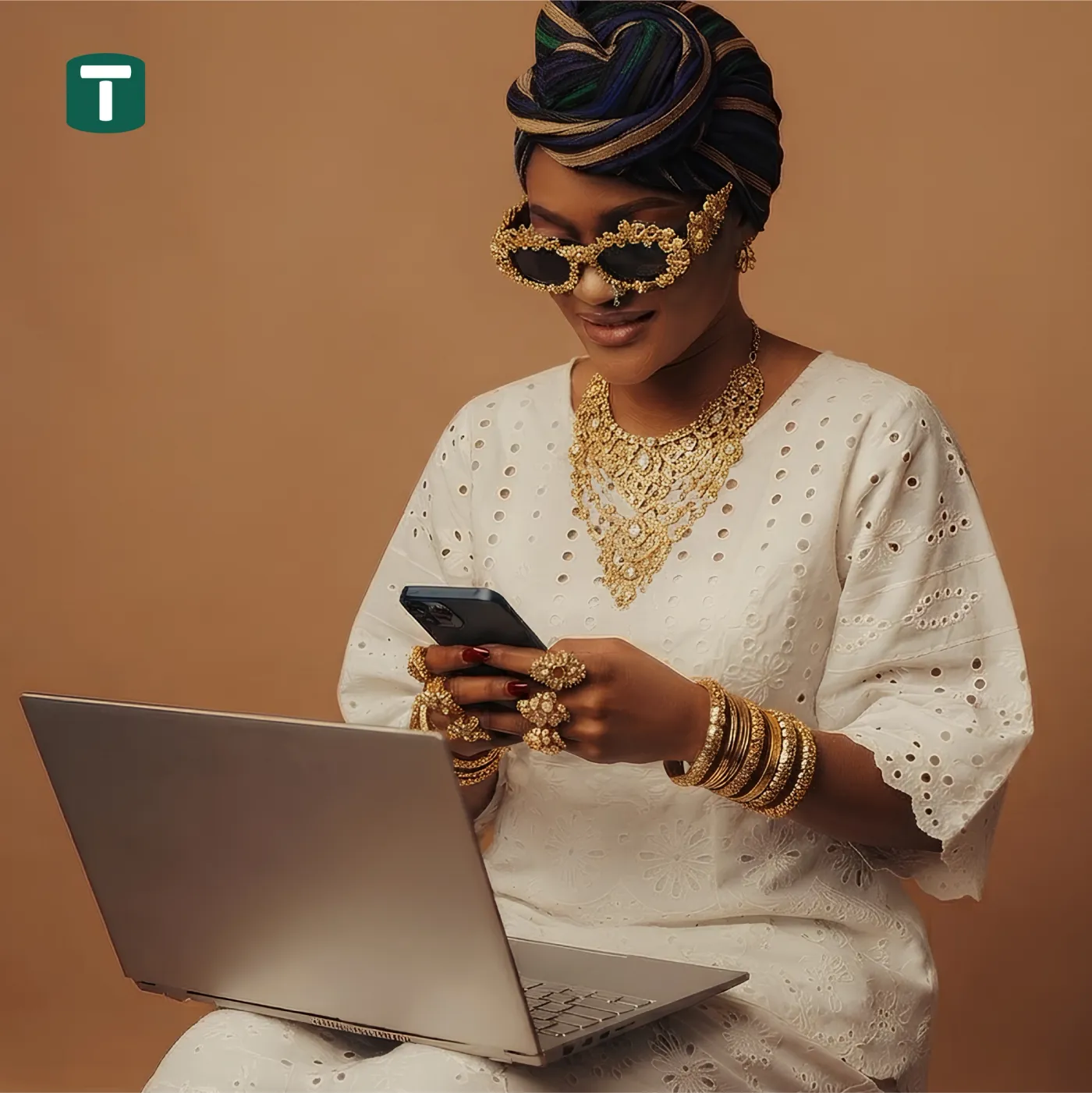 A woman in white eyelet fabric and gold jewellery using a phone beside a laptop, with the Tokkenly T mark.