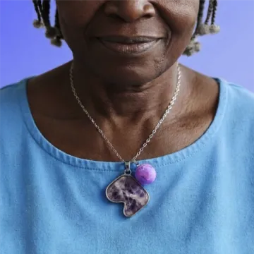 A woman in a blue top wearing the amethyst Safiri pendant, against purple.