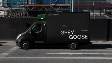 A black Grey Goose van parked outside a scaffolded building site, its side panel reading Work in progress