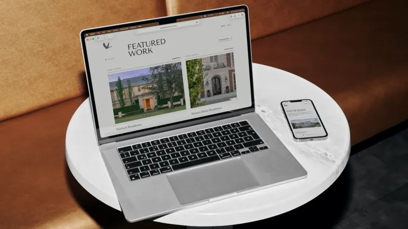 A laptop on a marble side table showing the Grey Goose featured work page, with a phone beside it open on the mobile site