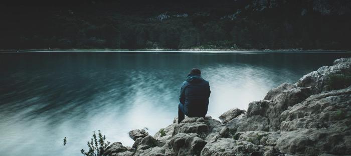 man sitting on rocky cliff overlooking body of water