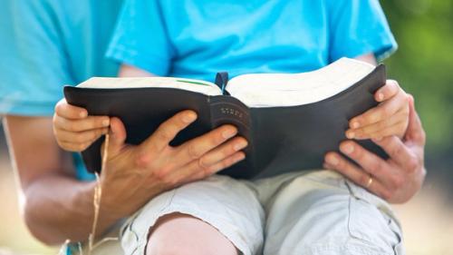 A father reading a Bible with his son in his lap.