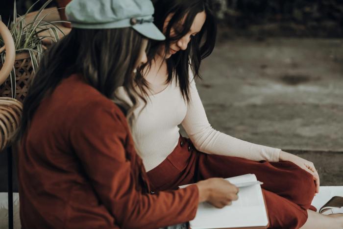 CC- two women with long dark hair sit side-by-side sharing a Bible