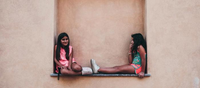 two girl in pink and green shirts sitting on wall shelf