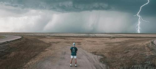 a person standing on a dirt road with lightning striking the ground