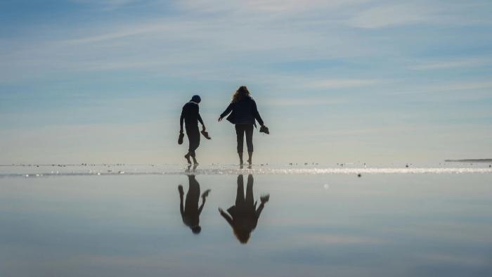 Two people walking barefoot on the sand with a reflection