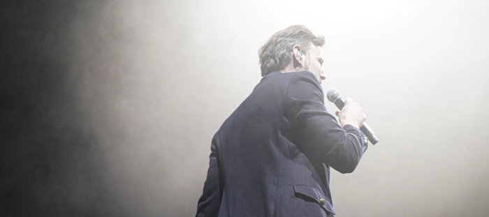CC- white male with ear piece holding a wireless microphone wearing a navy blue sport coat.