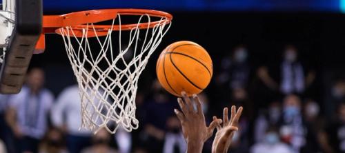 The hands of a basketball player putting a ball through the hoop.