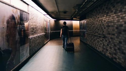 A person walking away down a hallway with a suitcase in tow.