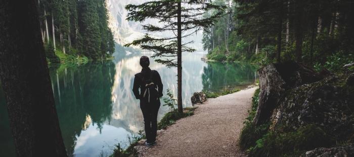 A woman hiking overlooking a lake with reflection of green trees and mountains in distance