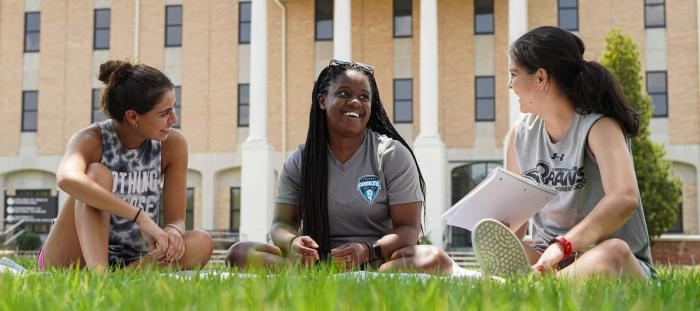 a group of women sitting on the grass in front of a building