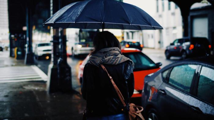 A woman walking along a street holding an umbrella on a dark, rainy evening.