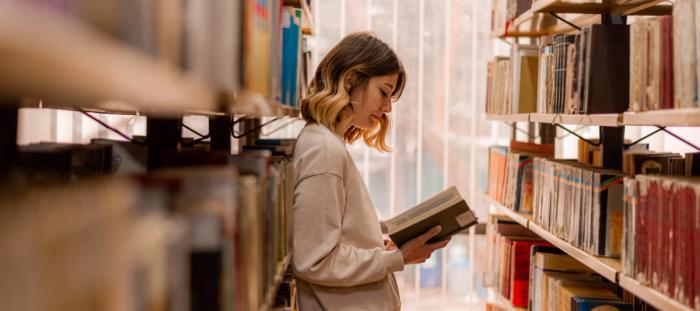 A woman reading a book in a library aisle
