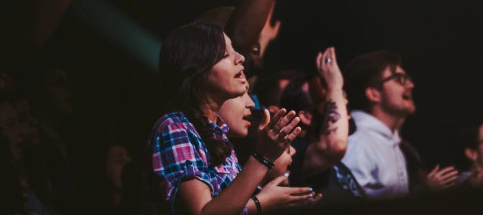 woman in plaid shirt in crowd lifting hands and singing