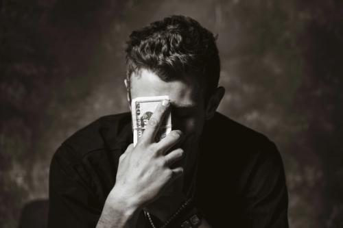 CC- a dramatic black & white portrait of a young man holding a wad of $20 bills up to his forehead in apparent despair.