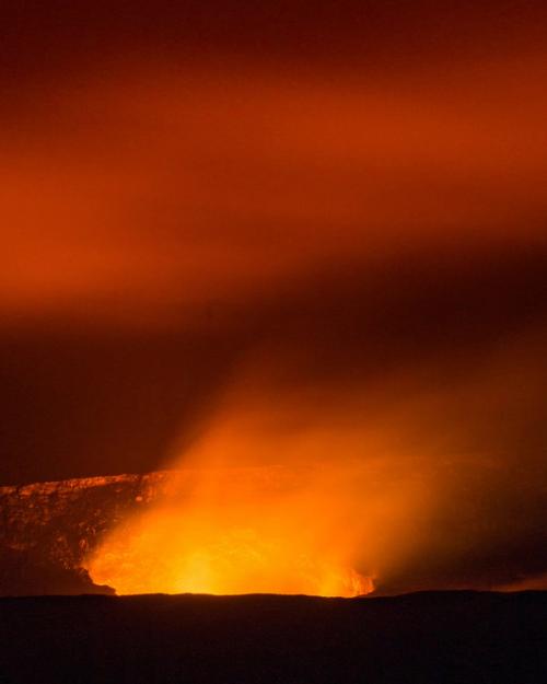 CC- Bright orange flames rise out of a volcanic opening into a hazy red sky.