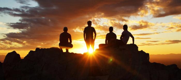 4 boys standing up on a rock in the sunset