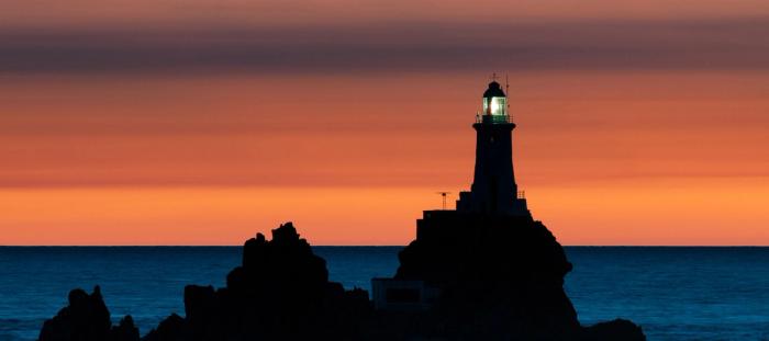 lighthouse on rocky outcropping at sunset 