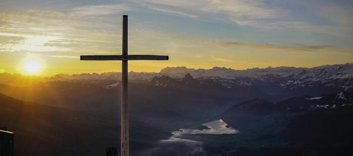 sun rising over mountains with giant wood cross in view