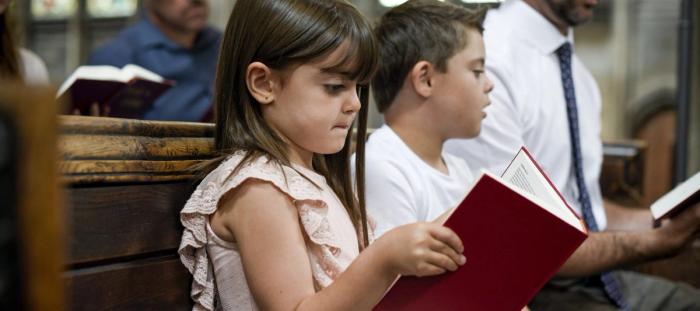little girl and boy sitting in pew of church reading