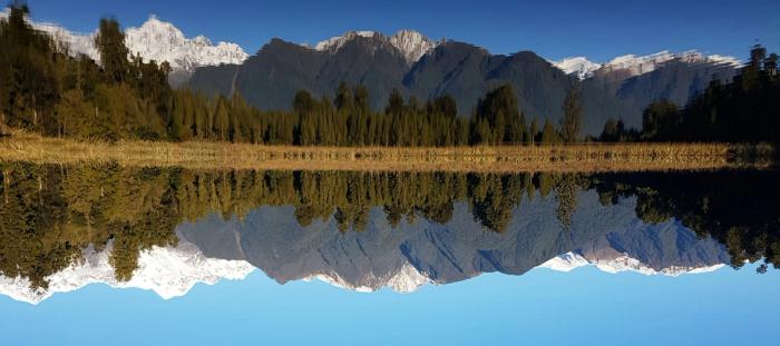 daytime view of reflection of snowy mountains and green trees in body of water