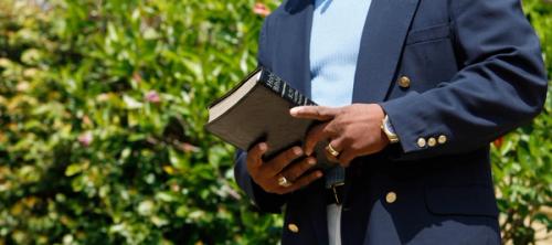 A man in a navy suit holding a bible in both hands.
