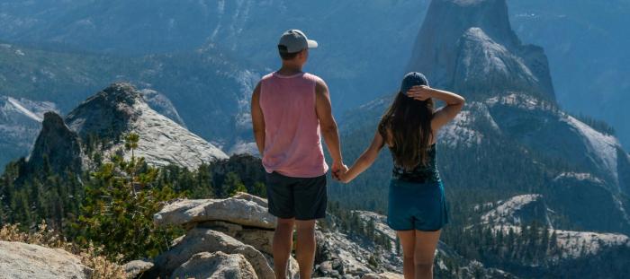 A man and woman holding hands while looking out over a forested mountain valley