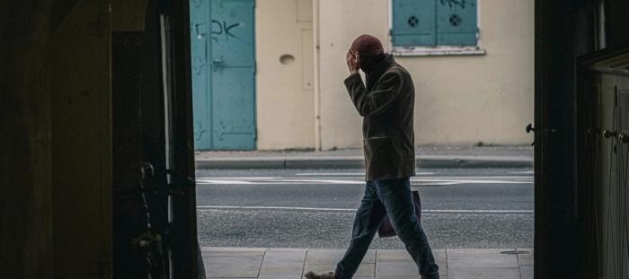 man in black jacket and blue denim jeans standing on sidewalk during daytime