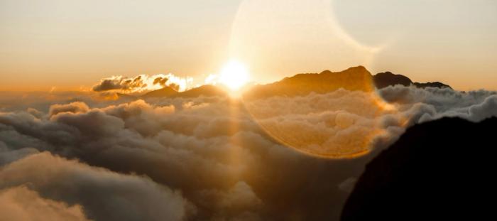 the sun setting over clouds and a mountain peak