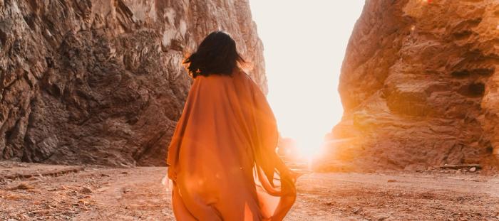 Woman in orange cloak walking into sunset on beach