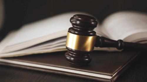 A judge's gavel resting on a book with an open book behind it.