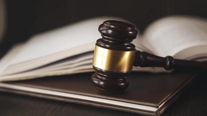 A judge's gavel resting on a book with an open book behind it.