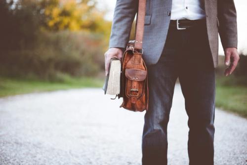 CC- A man dressed in a nice suit jacket and jeans walks down a road holding a Bible.