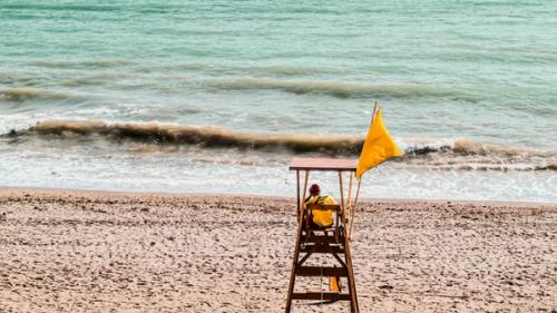 A lifeguard sitting in his tower at the ocean shore with a yellow flag flying.