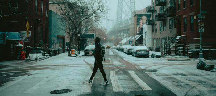 A hooded man walking across a rainy intersection