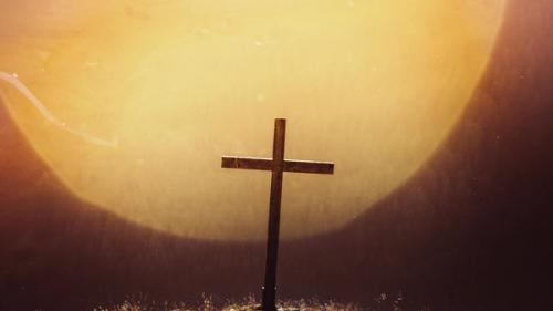 CC- a gigantic, slightly desaturated yellow sun and brownish-black sky fills the background and silhouettes a wooden cross, slightly canted to the right, standing atop a hill with equally desaturated yellowed grass seeming to glow with the light of the sun,