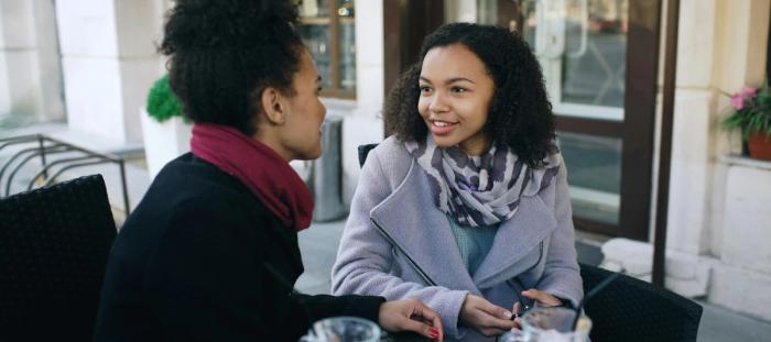 Two young women talking together in a cafe setting.
