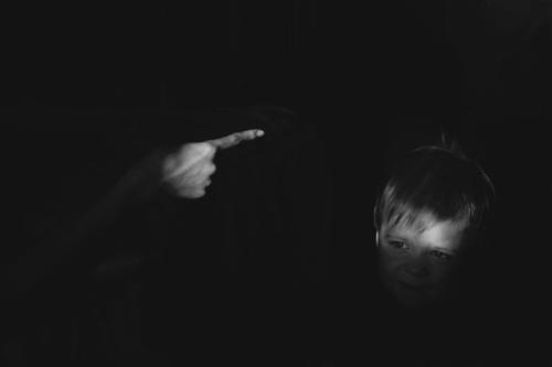 CC- a small boy with a distressed look on his face looks toward the finger of an adult point at him in condemnation.