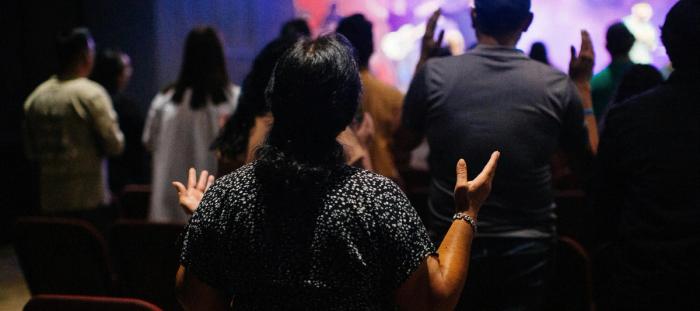 A crowd of people holding their hands up in praise at a contemporary worship service